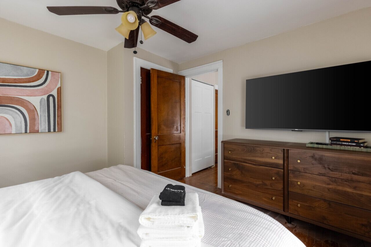 A hotel room with a bed, a wooden dresser, a flat-screen TV, and a ceiling fan.