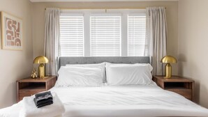 A neatly made bed with white linens, two bedside lamps, and a framed picture on the wall. - Stunning 3BR - Near Cleveland Clinic Main Campus (Cleveland Heights)