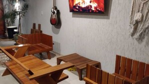 A cozy living room with wooden furniture, a TV mounted on the wall, and a guitar hanging on the wall. - Casa Refúgio das Águias na Praia do Preá (Cruz)