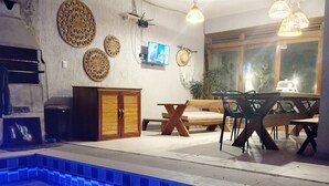 A pool area with tiled flooring, a wooden table and chairs, and decorative wall hangings. - Casa Refúgio das Águias na Praia do Preá (Cruz)