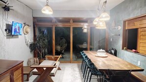 A modern dining area with a wooden table and chairs, a TV mounted on the wall, and a large window with a view of the outdoors. - Casa Refúgio das Águias na Praia do Preá (Cruz)