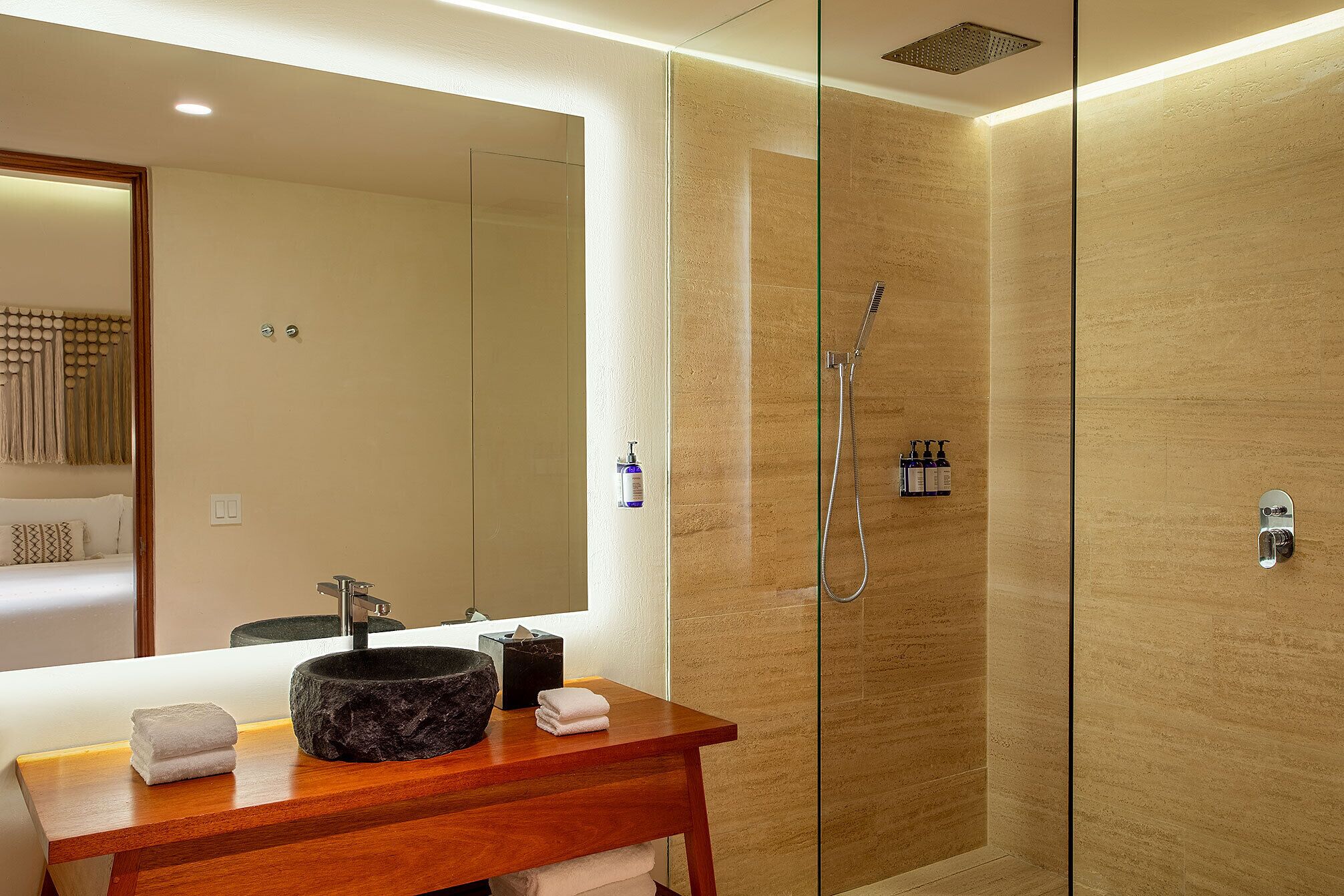 Un baño moderno con ducha acristalada, tocador de madera con lavabo de piedra y un espejo grande.