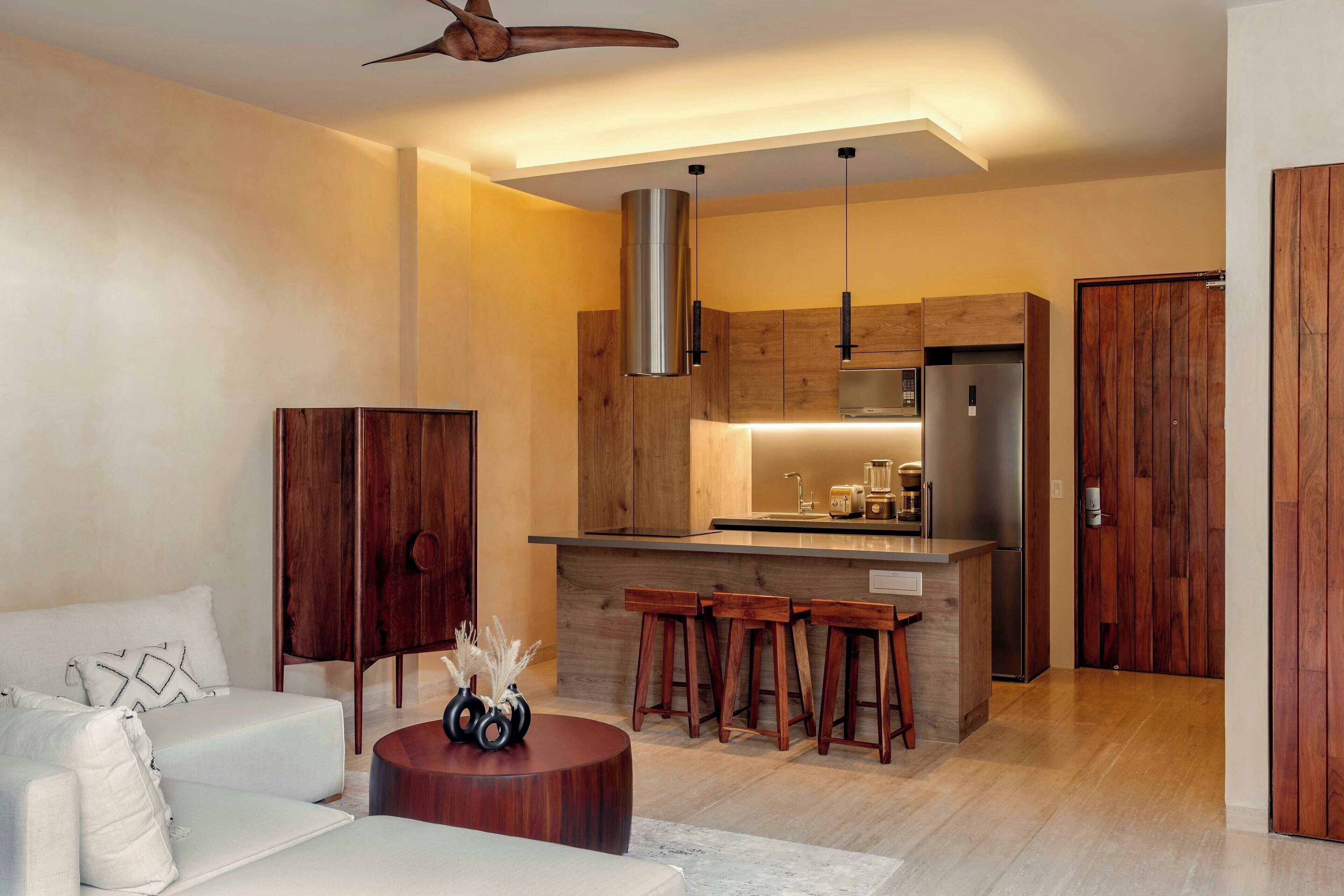 A modern kitchen with wooden cabinets, a stainless steel refrigerator, and a bar area with stools.