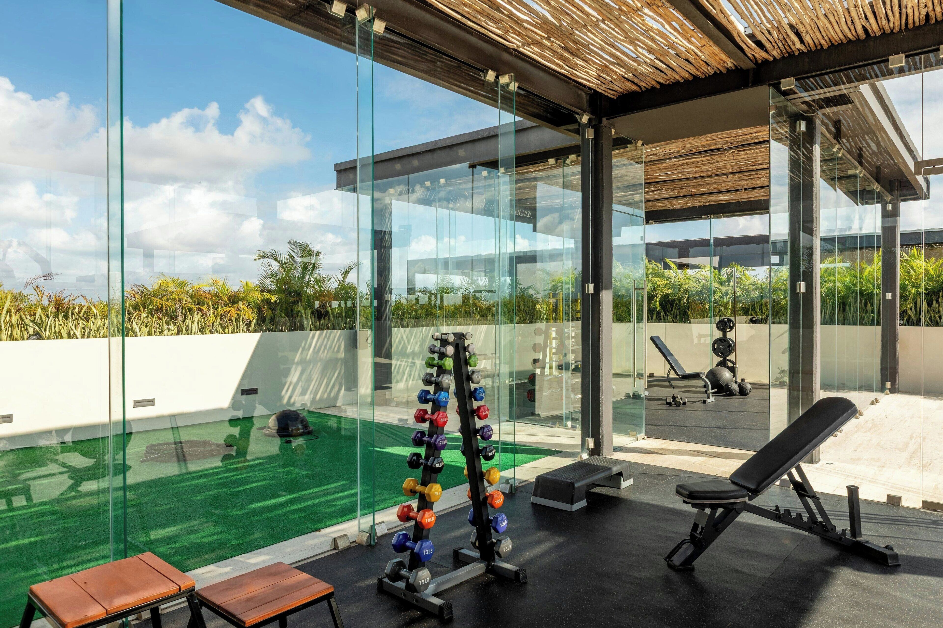 A modern gym with a glass wall, outdoor seating, and a weightlifting rack.