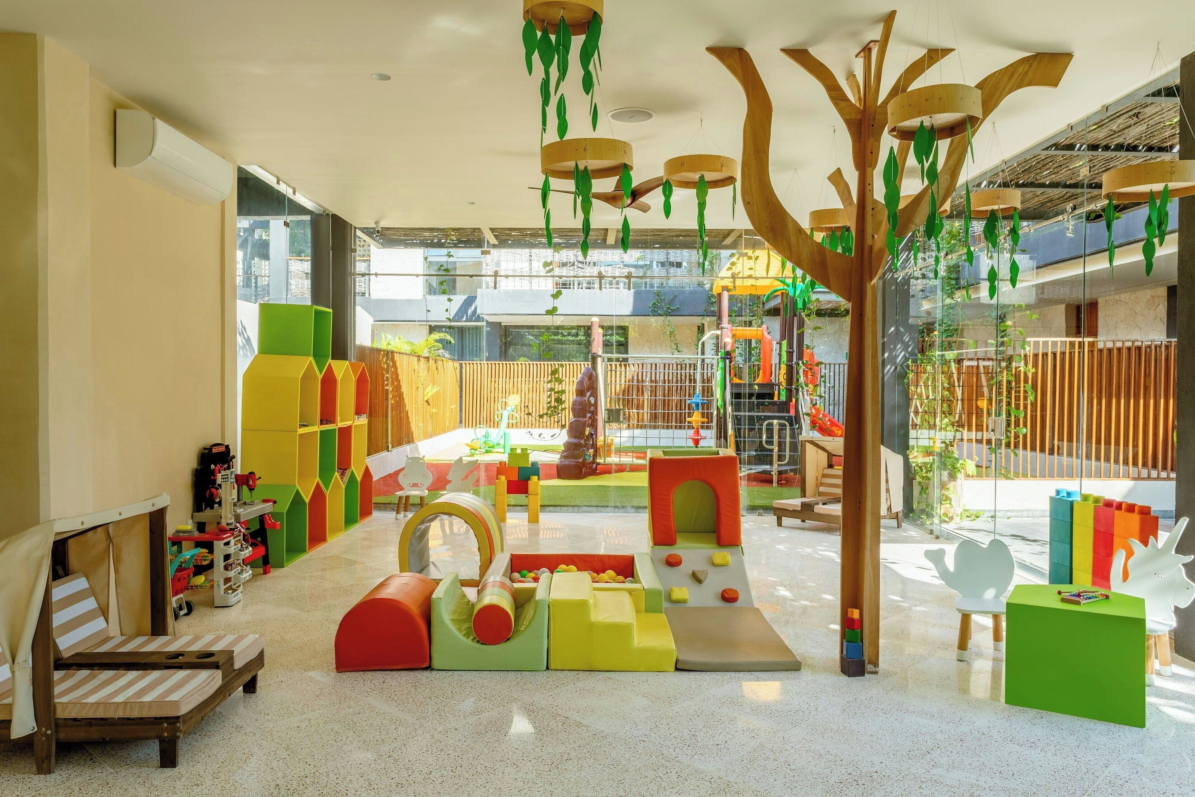 Un área de juegos infantiles con diversas estructuras de juego, una zona de estar con cojines y vistas al exterior.