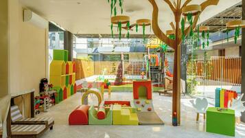 Un área de juegos infantiles con diversas estructuras de juego, una zona de estar con cojines y vistas al exterior.