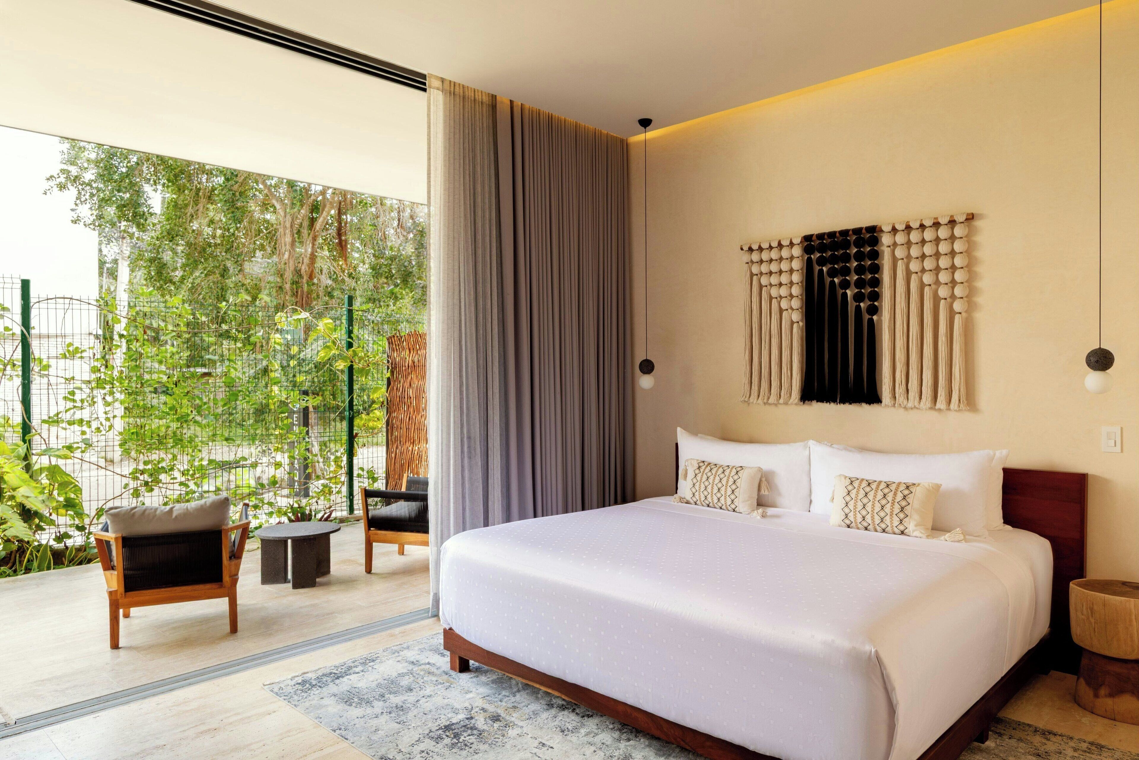 Un dormitorio moderno con una cama grande, vistas al verdor exterior y un balcón con mobiliario.