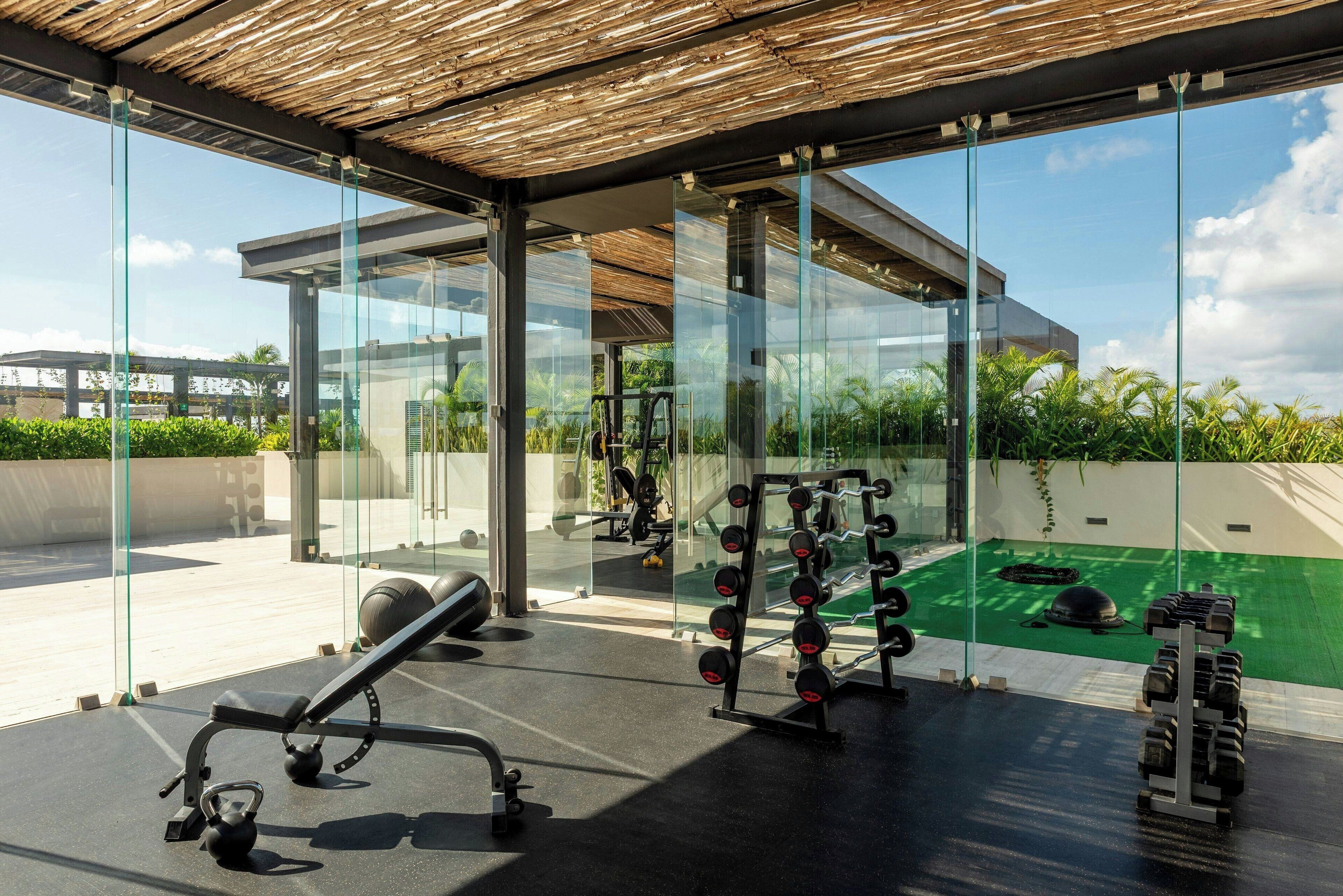 Un gimnasio moderno con paredes de vidrio, equipo de ejercicio y vistas al exterior.