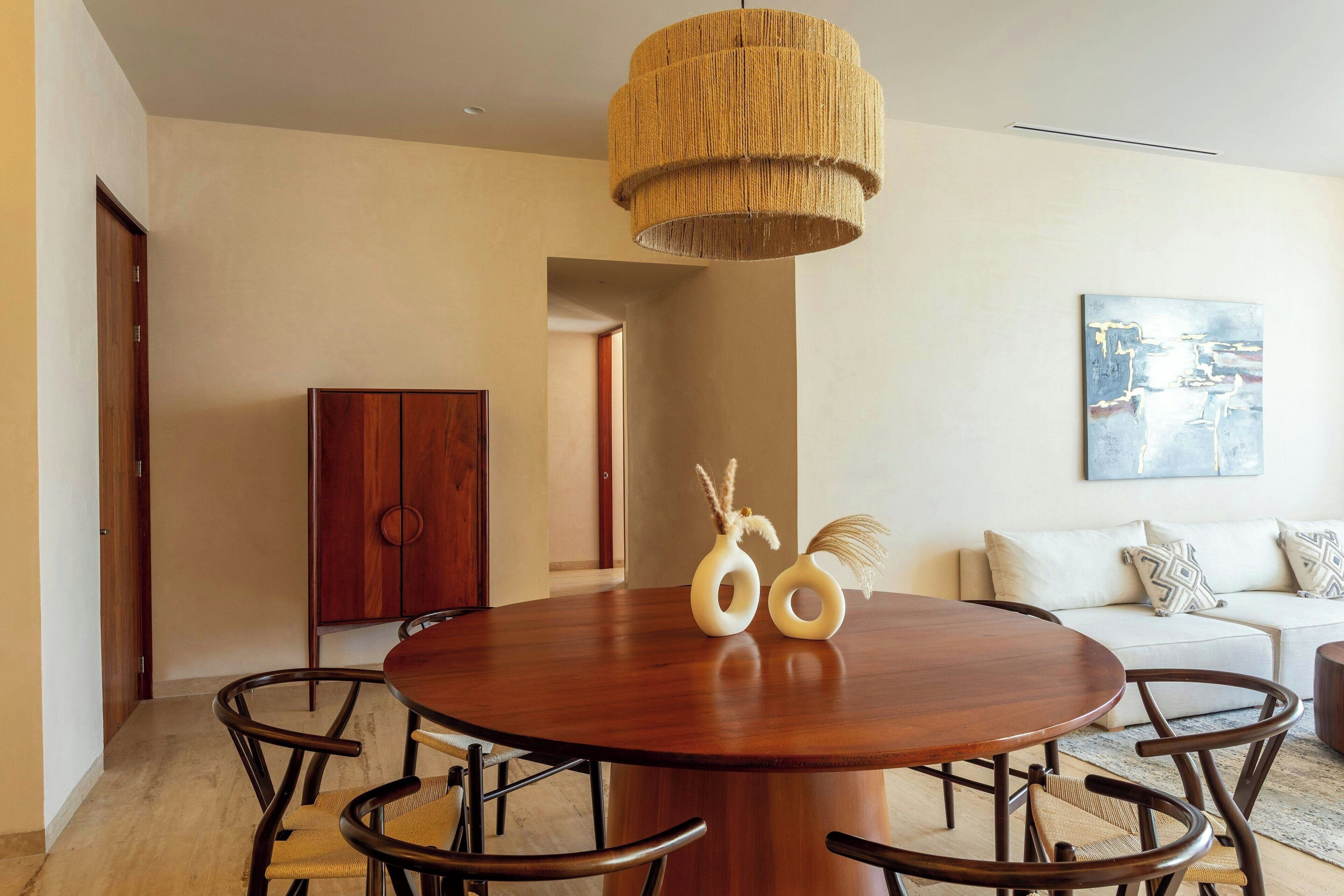 Un coin repas avec une table ronde en bois, six chaises et un luminaire suspendu.