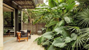Un patio al aire libre con un banco de madera, una mesa y exuberante vegetación tropical.