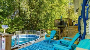 An outdoor swimming pool with a wooden deck, blue chairs, and a wooden deck area with a ladder. - Fun & Cozy Retreat: Nature & Games (Quinte West)