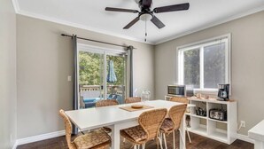 A dining area with a white table and wicker chairs, a ceiling fan, and a view of the outdoors through large windows. - Fun & Cozy Retreat: Nature & Games (Quinte West)