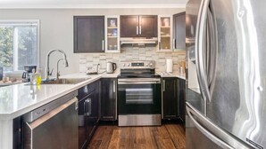 A modern kitchen with dark cabinetry, stainless steel appliances, and a large refrigerator. - Fun & Cozy Retreat: Nature & Games (Quinte West)