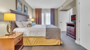 Ein Hotelzimmer mit einem Bett, Nachttischlampen, einem Schminktisch, einem Fernseher und einer Tür.