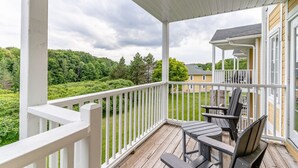 Ein überdachter Außenbereich mit Holzterrasse, weißen Geländern und zwei Stühlen.