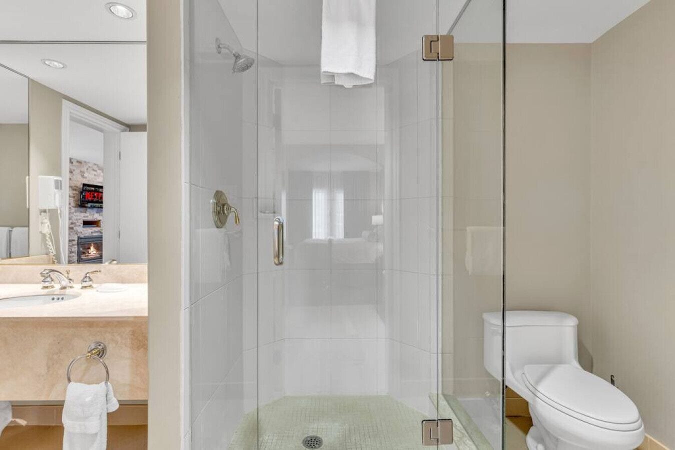 Un baño moderno con ducha envuelta en vidrio, inodoro blanco y tocador con lavabo y espejo.