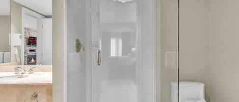 Un baño moderno con ducha envuelta en vidrio, inodoro blanco y tocador con lavabo y espejo.