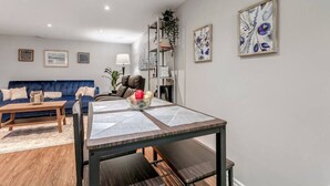 A modern living room with a blue sofa, a wooden coffee table, and a dining table with a geometric table runner.