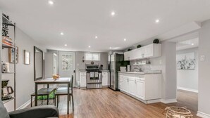 A modern kitchen with white cabinets, a dining area with a table and chairs, and a living room with a sofa and a decorative basket.