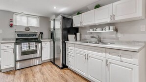 A modern kitchen with white cabinets, stainless steel appliances, and a wooden floor.