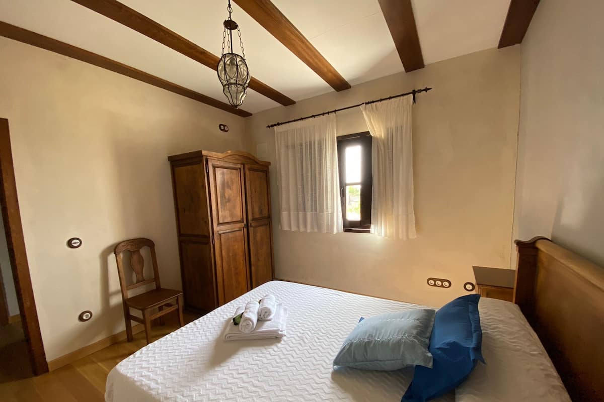 Un dormitorio con cama, armario de madera y ventana con cortinas.