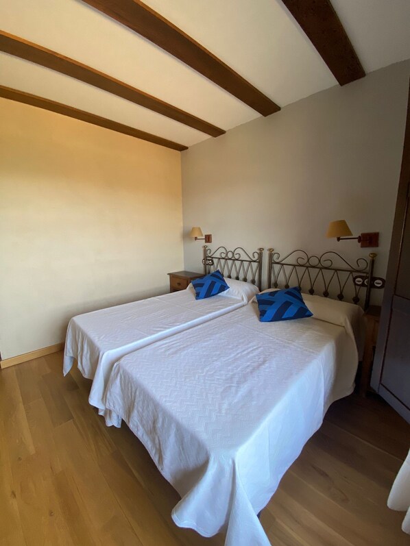 A room with two single beds, wooden flooring, a sloped ceiling with exposed beams, and two bedside lamps.