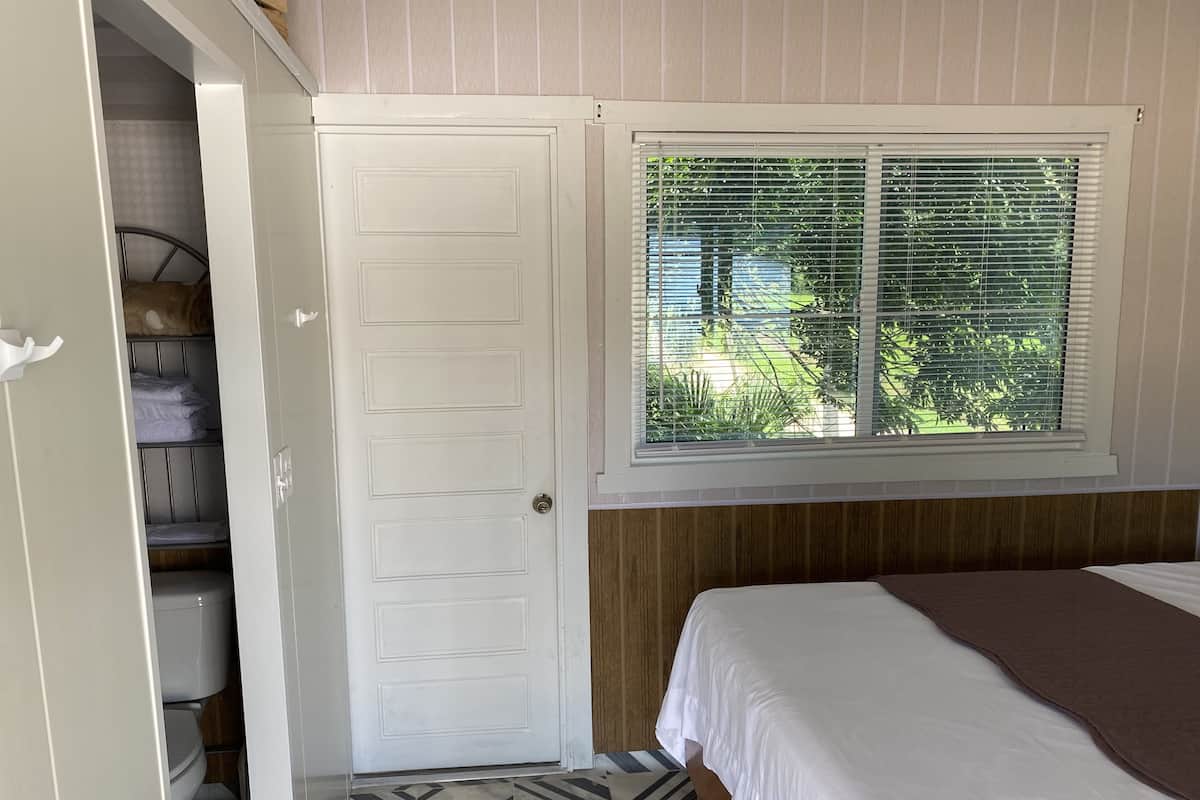 A bedroom with a bed, a window with blinds, a door, and a closet with shelves.