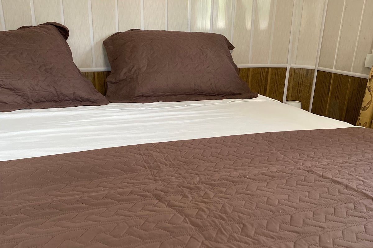 A bed with a brown quilt and two pillows.
