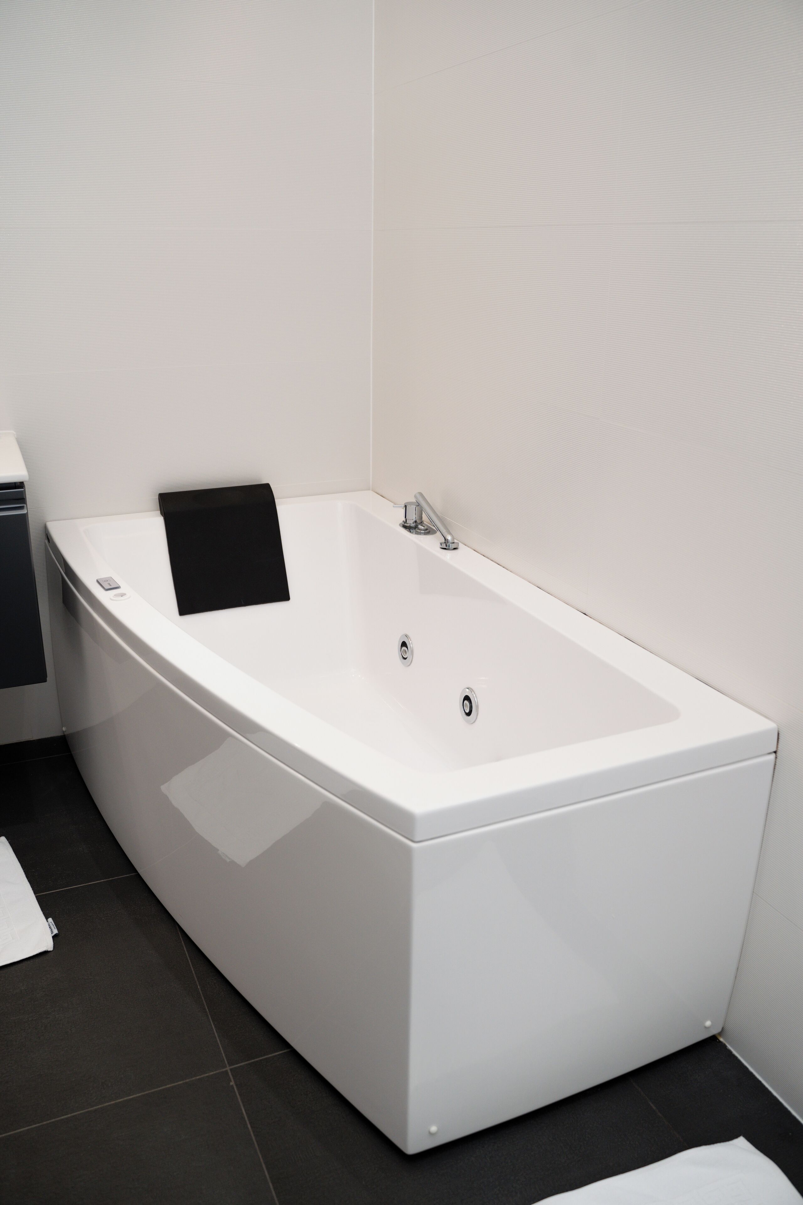 Een moderne badkamer met een witte badkuip, een zwarte handdoek en een witte wastafel.