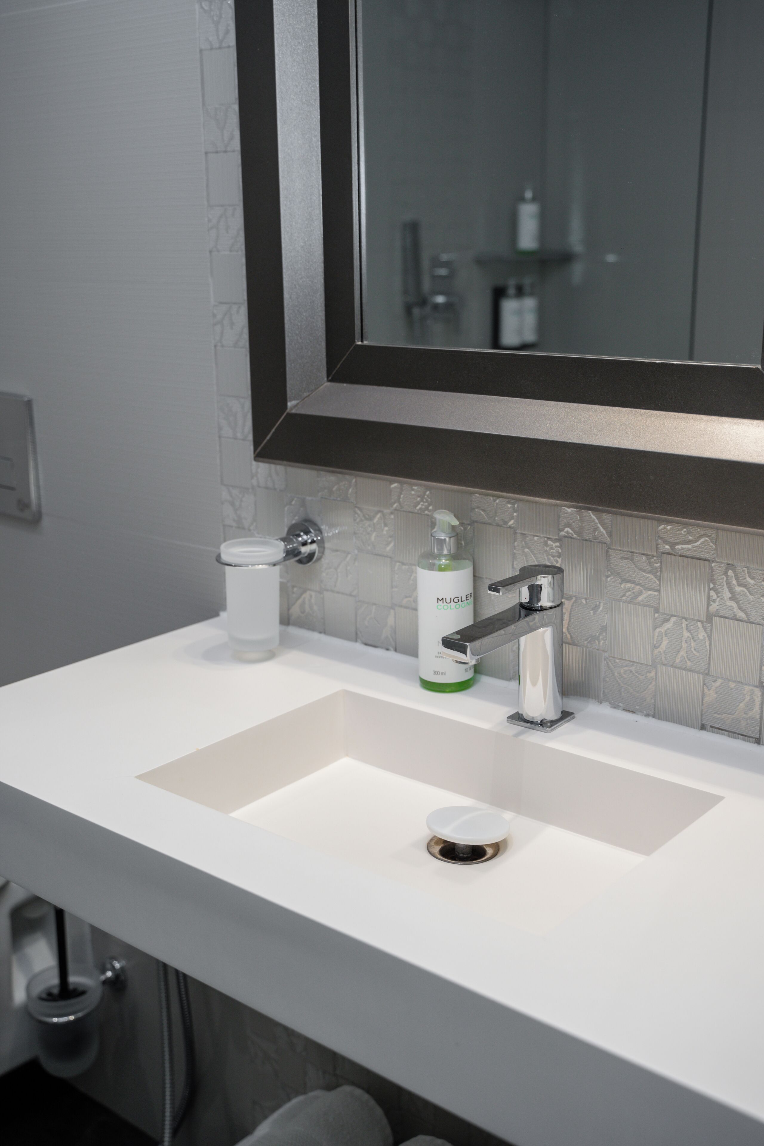 A bathroom with a white sink, a mirror, and a bottle of MUGGLE soap.