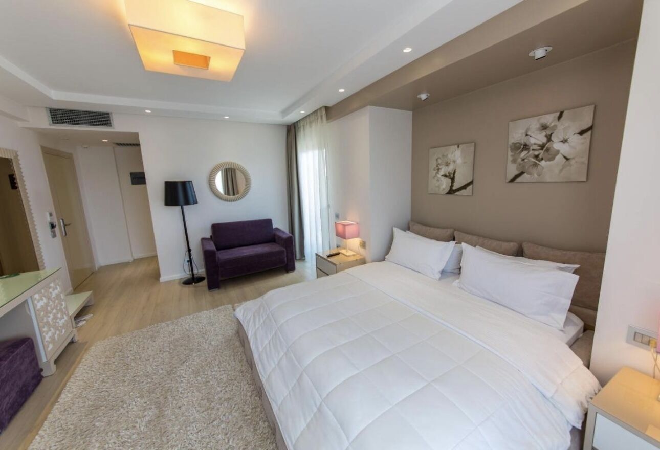 A modern bedroom with a large bed, a bedside table, a lamp, and a mirror.