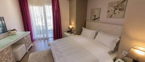 A hotel room with a large bed, a desk with a lamp, a TV, and artwork on the wall.