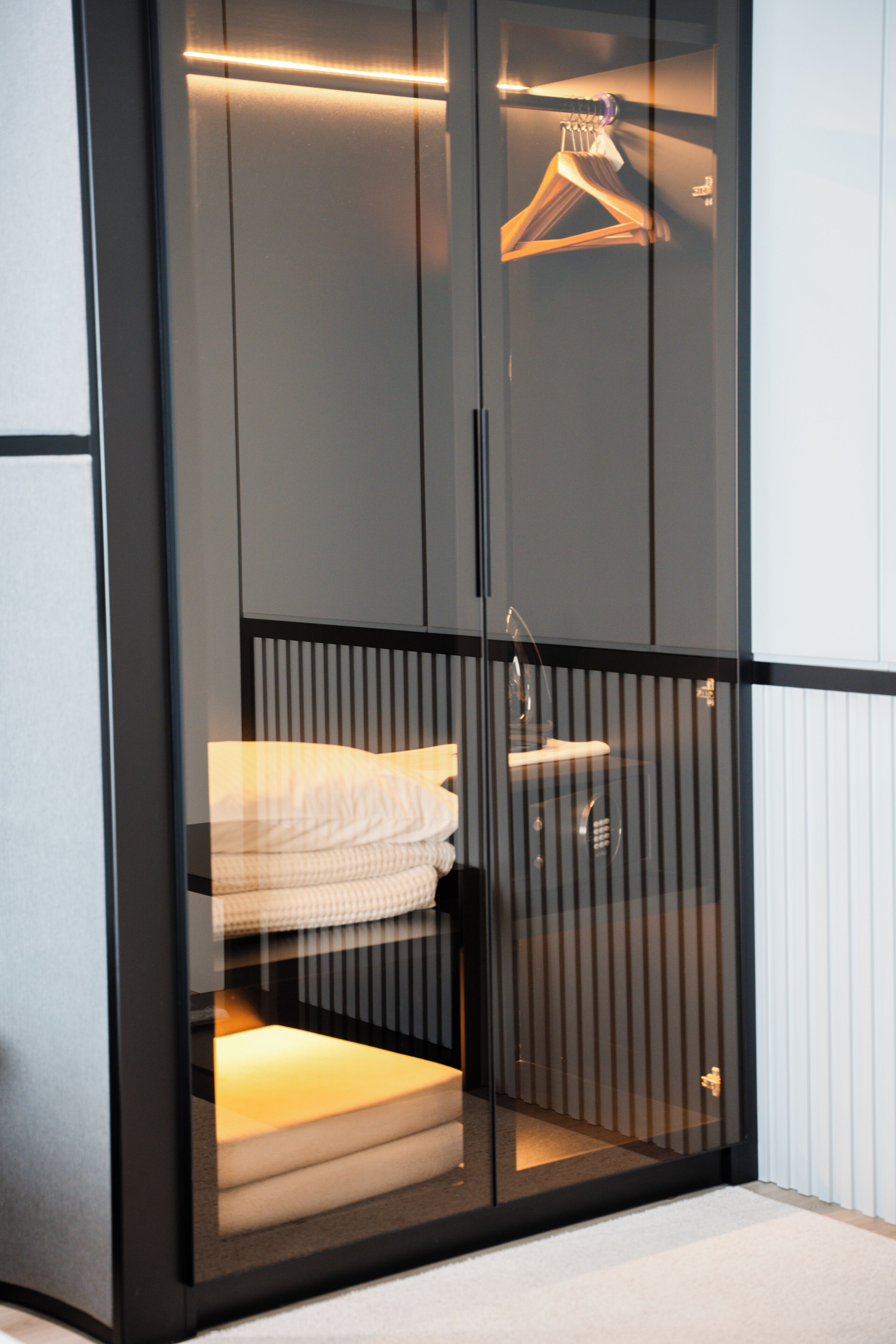 Un armario moderno con puerta de cristal, una barra para colgar ropa y una toalla doblada en su interior.