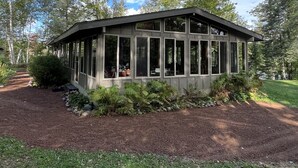 A modern, single-story building with large windows, surrounded by a well-maintained garden and trees. - Hot Tub in the Forest Cozy Home on Peaceful Lake (Mountain)