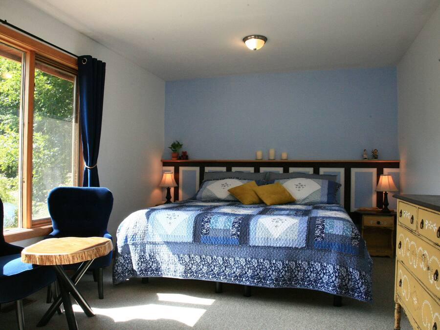 A bedroom with a bed, two chairs, a dresser, and a window with curtains.