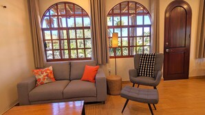 A living room with a grey sofa, an ottoman, a patterned armchair, and a wooden floor.