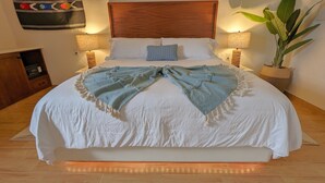 A neatly made bed with a white duvet and a blue throw blanket, flanked by two bedside lamps and a potted plant.