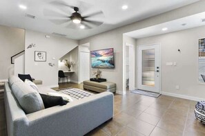 A modern living room with a sofa, a ceiling fan, a flat-screen TV, and a door with a glass panel. - Charming 4BR Near Fort Bliss (El Paso)