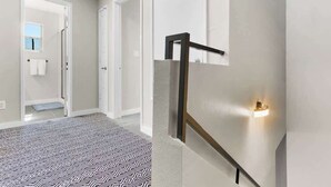 A hallway with a patterned carpet, a staircase with a handrail, and a wall-mounted light fixture. - Charming 4BR Near Fort Bliss (El Paso)