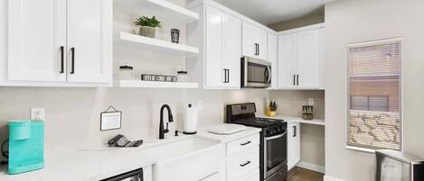 A modern kitchen with white cabinets, a microwave, stove, and a dishwasher.