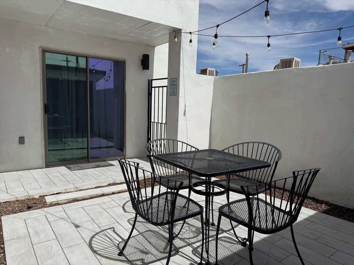 A patio with a table and chairs, a sliding glass door, and a white wall.
