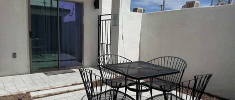 A patio with a table and chairs, a sliding glass door, and a white wall.