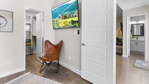 A hallway with a door, a chair, a rug, and a painting. - Charming 4BR Near Fort Bliss (El Paso)