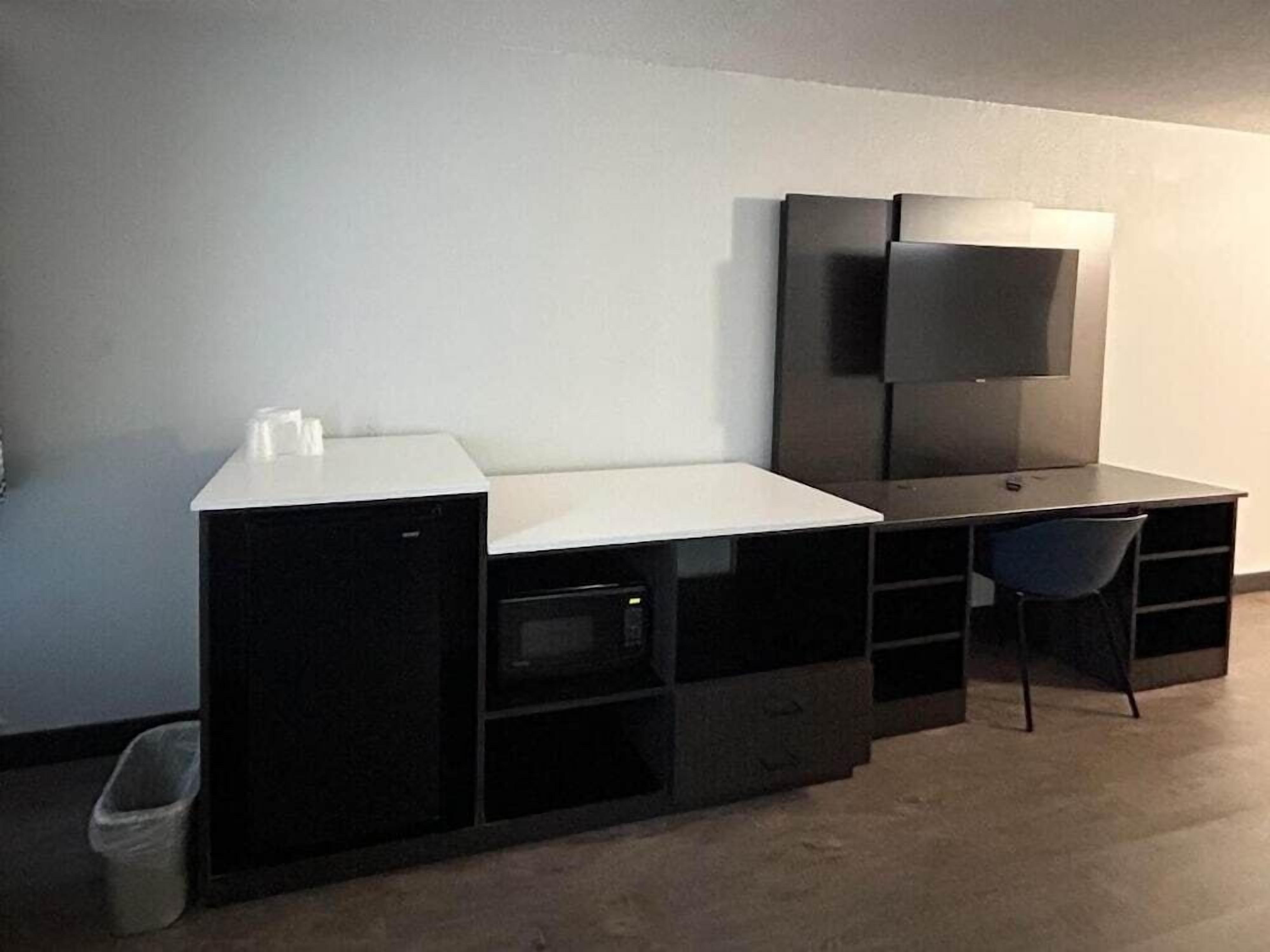 Een compacte, moderne kamer met een kitchenette, een flatscreen televisie aan de muur en een kleine stoel.