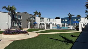 A modern hotel with a swimming pool, palm trees, and a well-maintained lawn. - Studio 6 Carson, CA (Carson)