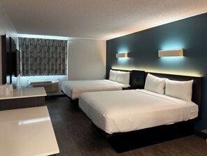 Habitación de hotel con dos camas, un escritorio, un ventanal con cortinas estampadas y una pared oscura con iluminación decorativa.