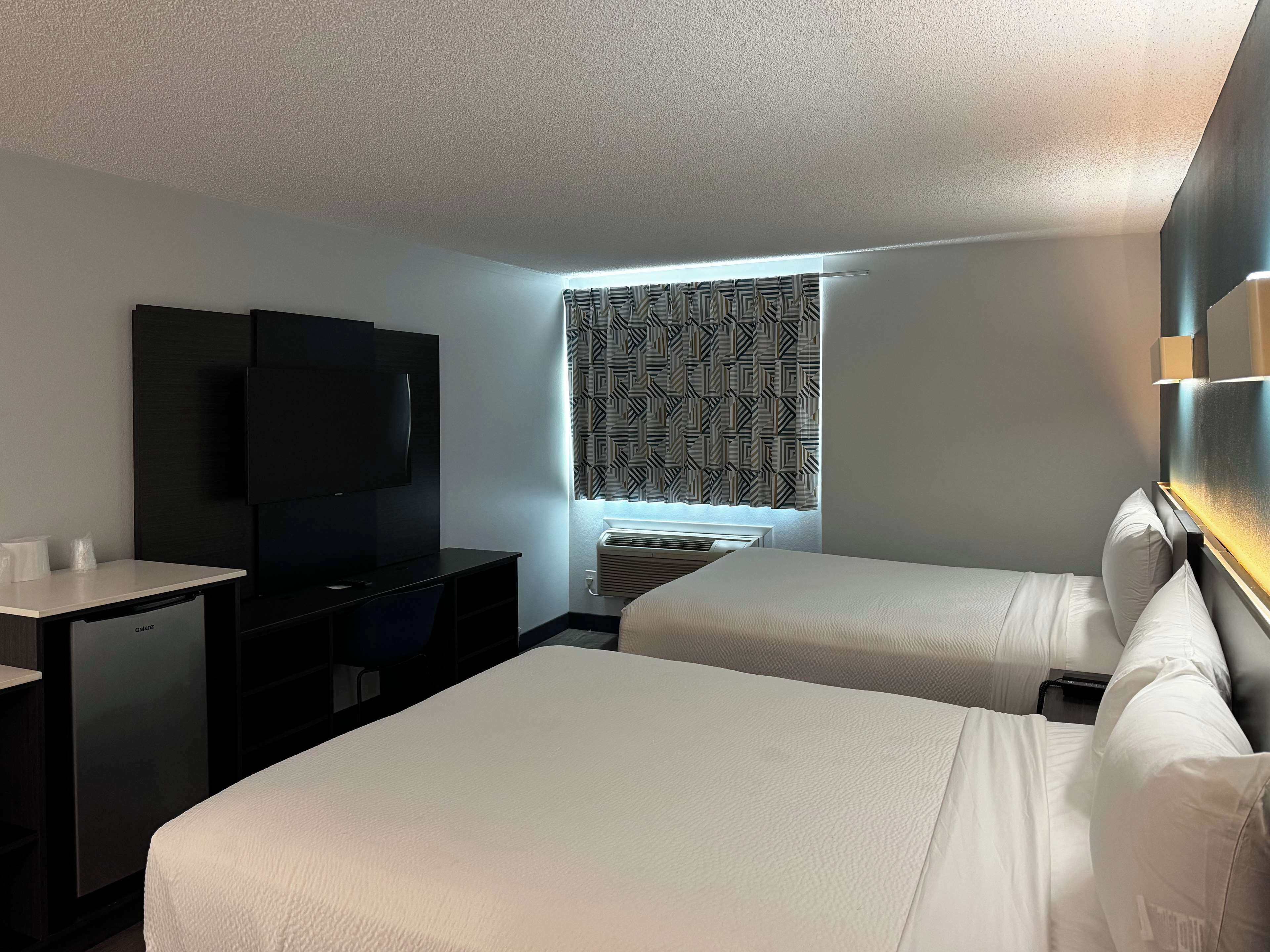 Una habitación de hotel con dos camas, un escritorio, un televisor y una ventana con diseño.