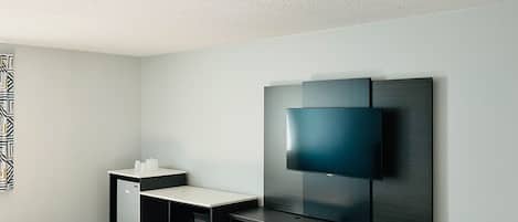 Habitación de hotel moderna con una cama grande, un escritorio, un televisor de pantalla plana, una kitchenette pequeña y una silla azul.