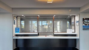 A reception desk with a modern design, featuring a glass partition and a digital display. - Studio 6 Carson, CA (Carson)