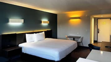 Ett hotellrum med en stor säng, sängbord, ett skrivbord och en stol. Det finns väggmonterade lampor och en dörr med en skylt.